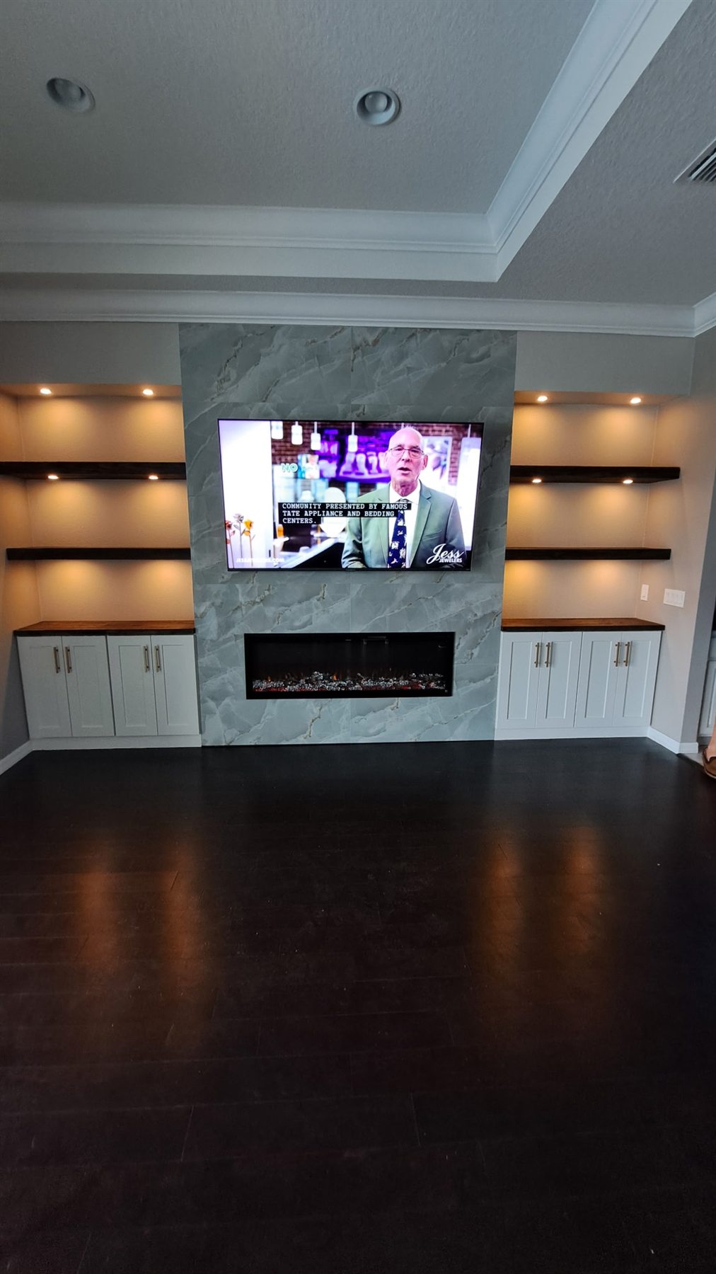 Custom marble-faced media wall with lit floating shelves and a linear fireplace