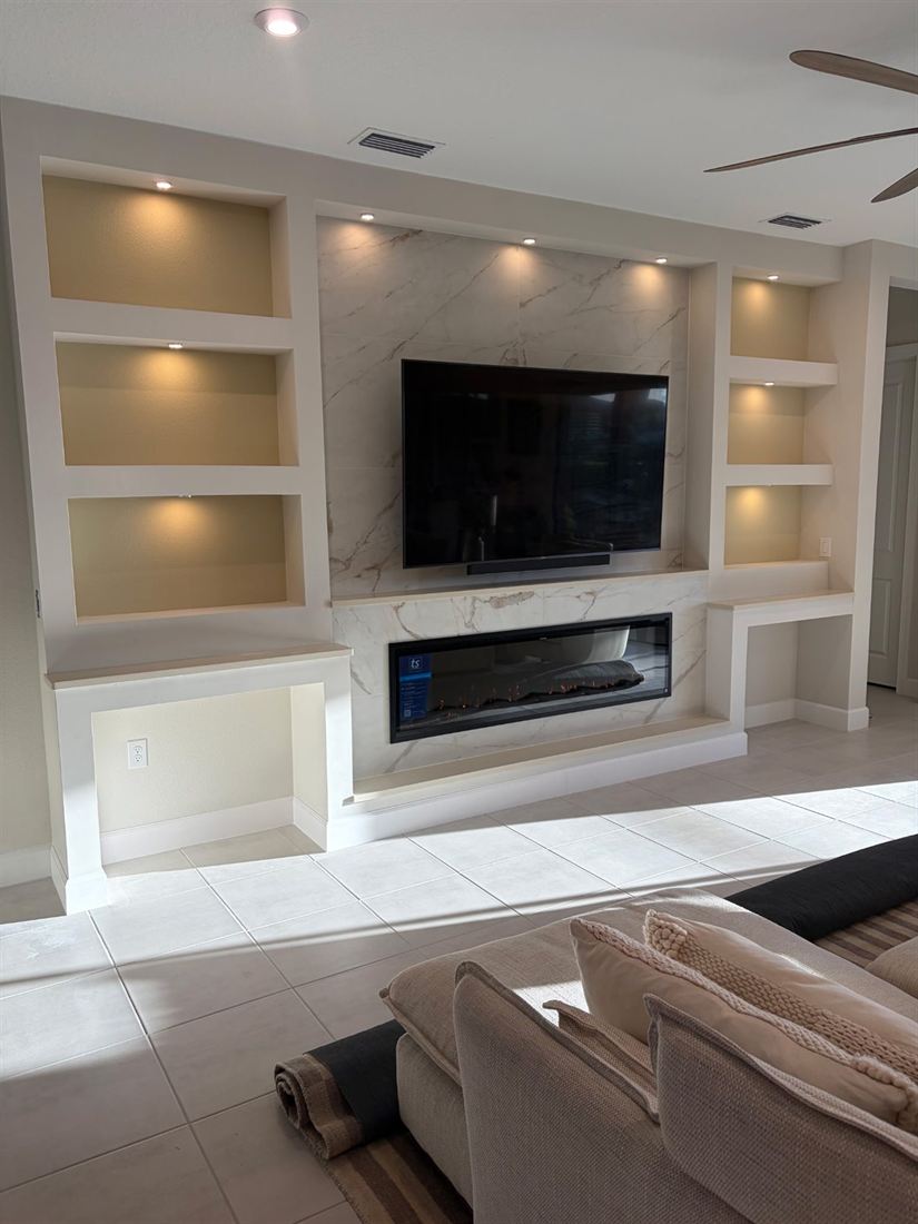White built-in media wall with marble backing, lit niches and fireplace